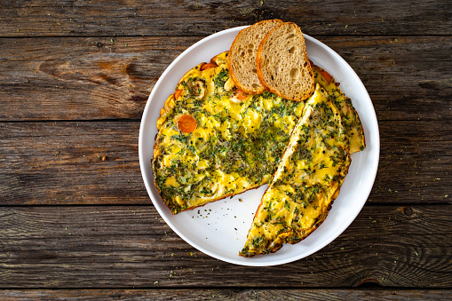 Omelette - scrambled eggs with cheese and vegetables on wooden table