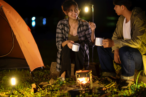 Two Teenager backpackers are sitting near camping stove, Boiled water for cooking delicatessen easy food. Camping in nature, Cooking at night with an atmosphere that is warm and romantic.
