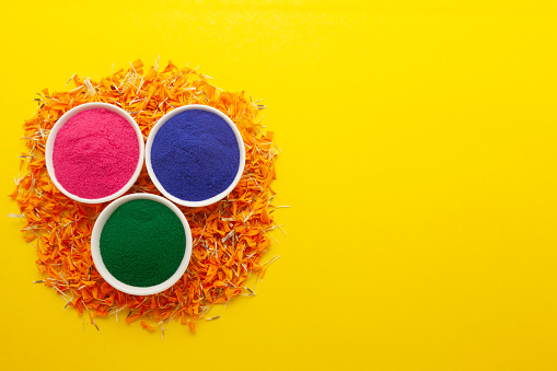 Top view of colorful traditional Rangoli powder in white bowls, on orange marigold petals.