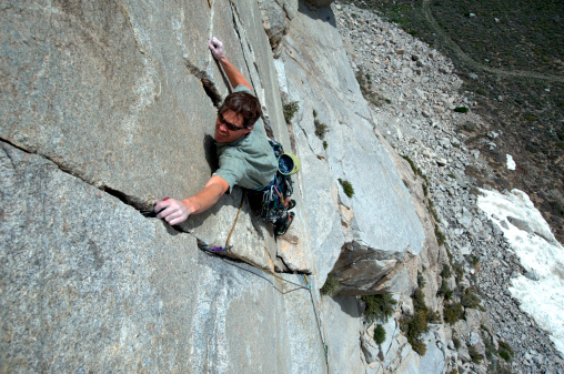 A rock climber stretches to place a piece of protection while climbing a granite wall in California.
