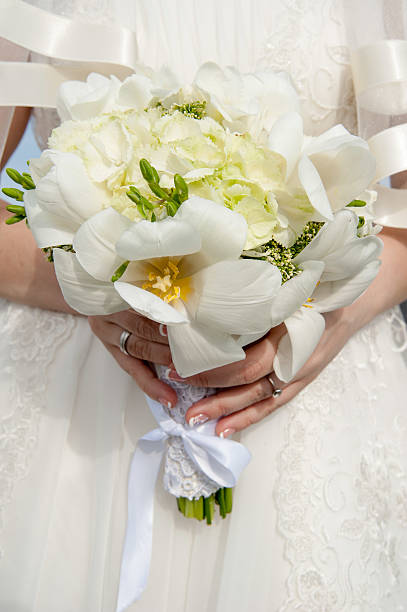 Hands of the groom hugging bride with wedding bouquet