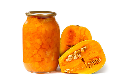 A jar of pumpkin jam with natural pumpkin halves. Canned pumpkin on white background.