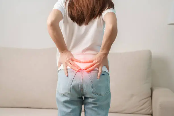 Photo of woman having back body ache during sitting on Couch at home. adult female with muscle pain due to Piriformis Syndrome, Low Back Pain and Spinal Compression. Office syndrome and medical concept