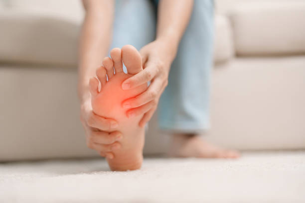 frau mit barfußschmerzen beim sitzen auf der couch zu hause. fußschmerzen durch plantarfasziitis und langes aufwachen. gesundheits- und medizinkonzept - fuß anatomiebegriff stock-fotos und bilder