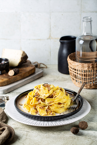 Truffle fettuccine with mushrooms, long egg pasta. Italian first course made with hard cheese and butter. Ripe whole truffles and loaf of cheese on background.