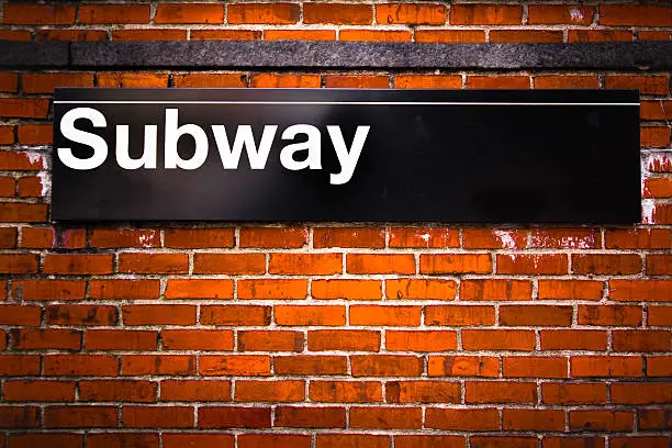 Photo of Sign for the subway on a brick wall