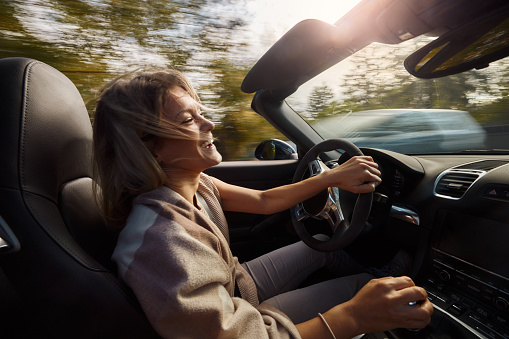 Young cheerful woman enjoying while driving a convertible car. Blurred motion.
