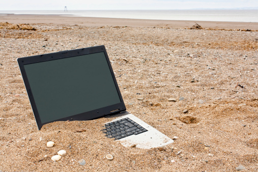 old or obsolete unwanted laptop on the beach with blank screen for your own message good concept for unwanted technology or travel websites