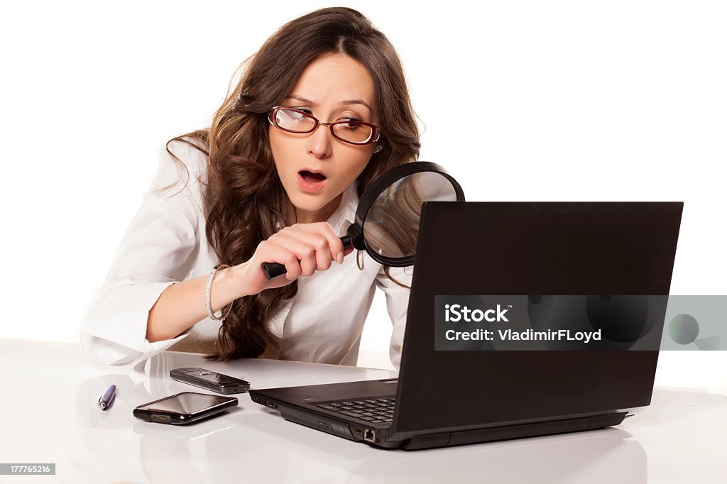 A younger businesswoman uses a spyglass suspicious secretary in white shirt did found something on her laptop with a magnifying glass Magnifying Glass Stock Photo