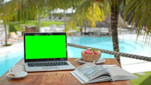 Photo of Croma key computer closeup. Green screen backdrop. Macbook laptop palm tree cafe