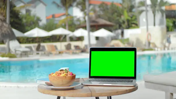 Photo of Green screen macbook display. Chroma key laptop near swim pool. Computer monitor
