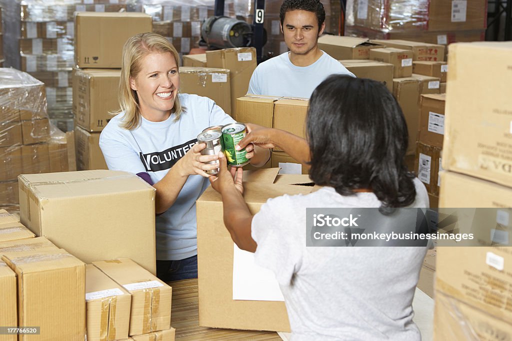 Volunteers collecting food donations in a warehouse Volunteers Collecting Food Donations In Warehouse Smiling Food Bank Stock Photo