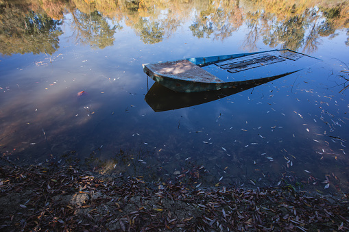 Autumn scene from river, fading trees reflecting at blue water surface at sunny autumn day with submerged small boat in foreground, no people