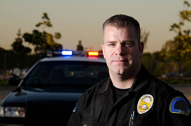 Evening head shot of male police officer with car behind A K9 police officer standing in front of his patrol car while wearing a BDU uniform. police dog handler stock pictures, royalty-free photos & images