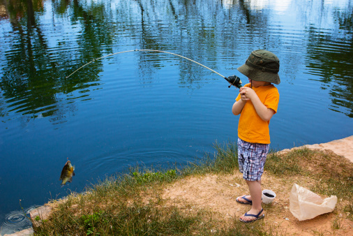 A cute little boy reeling in a big fish.