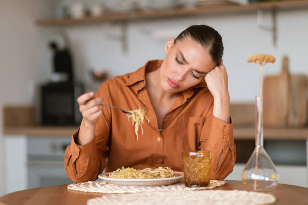 Young caucasian sad woman sitting at table in kitchen interior, looking at homemade pasta and dont want to eat Young caucasian sad woman sitting at table in kitchen interior, looking at homemade pasta and dont want to eat, needs to keep diet dont eat meat stock pictures, royalty-free photos & images