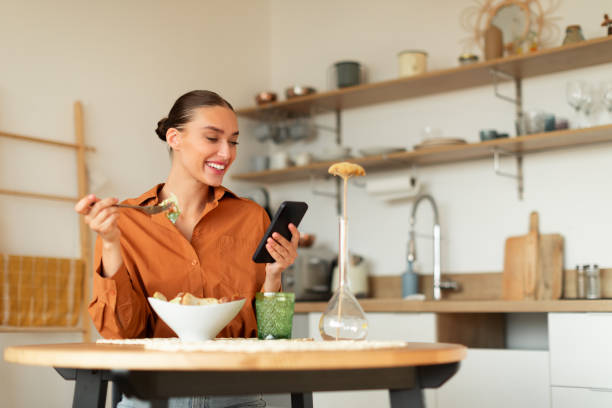 istock Cheerful lady eating tasty salad and using cellphone, sitting at table in kitchen while having dinner, copy space 1777755425