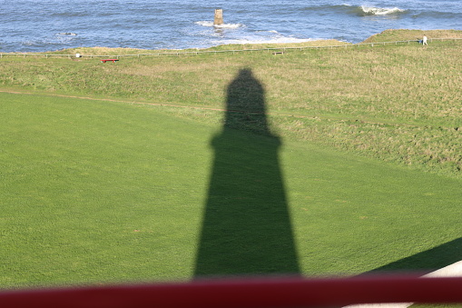 Shadow of a tall lighthouse on the grass below