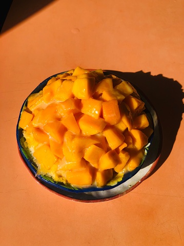 A bowl filled with freshly-cut mango slices atop an orange table, ready to be enjoyed