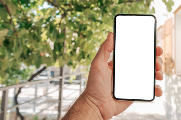 istock Man holding smartphone with blank white mockup screen in house back yard 1777774458