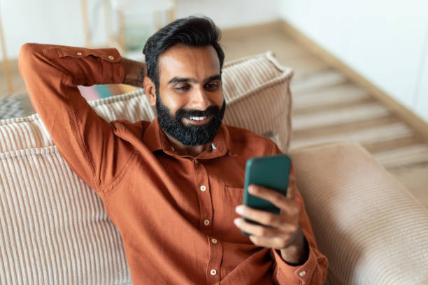 istock Cheerful Indian Bearded Guy Texting Using Phone In Living Room 1777777842