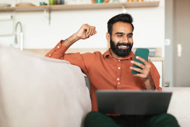 istock Joyful Eastern man shaking fist reading message on smartphone indoor 1777778430