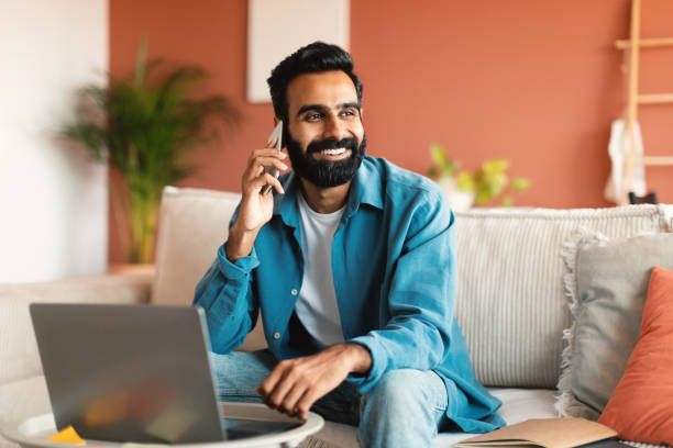 istock Cheerful indian man with laptop communicating on phone at home 1777780215