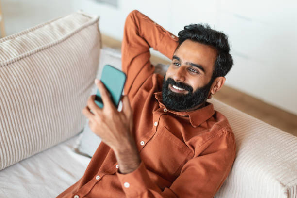 istock Happy arab man holding mobile phone leaning on sofa indoor 1777780238