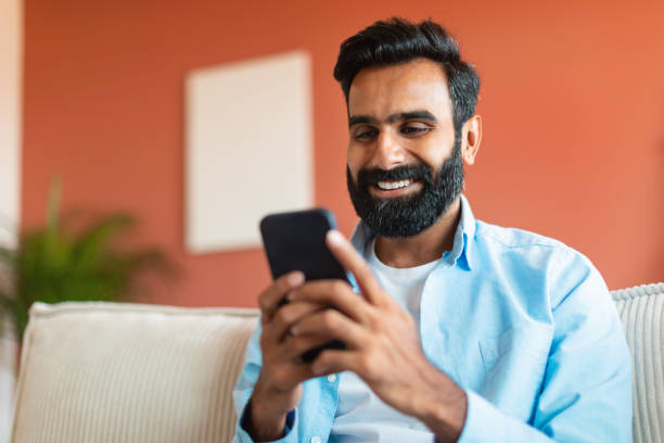 istock Cheerful Indian Man Using Mobile Phone Surfing Internet Sitting Indoor 1777780243