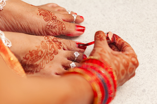 Beautiful Indian bride applying red nail polish on her nails carefully.