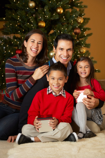 Family In Front Of Christmas Tree Opening Presents Smiling To Camera