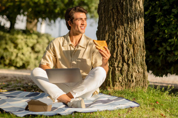 istock Happy man have picnic at park, using laptop, eating sandwich 1777829182