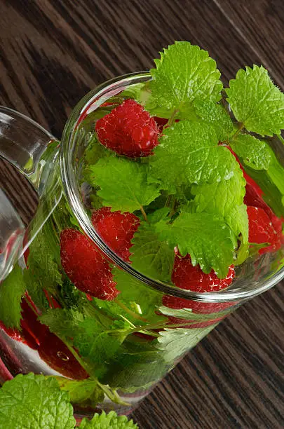Glass Cup of Raspberry Beverage with Perfect Fresh Lemon-Balm Leafs on Dark Wooden background