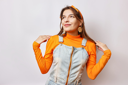A beautiful cheerful girl poses in front of the camera in a denim suit and an orange T-shirt.