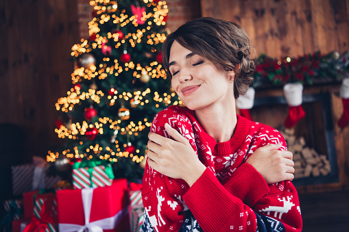 Portrait cute girl wear red sweater evergreen xmas tree cuddle herself closed eyes comfortable new year holiday isolated indoors background.