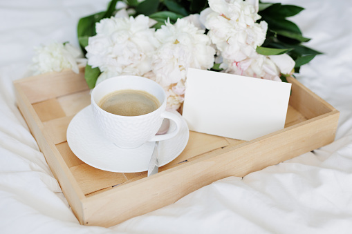 Romantic morning, coffee in bed with peony flowers on tray with blank card
