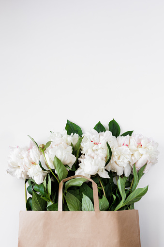 Beautiful white peonies and leaves in brown paper bag with copyspace
