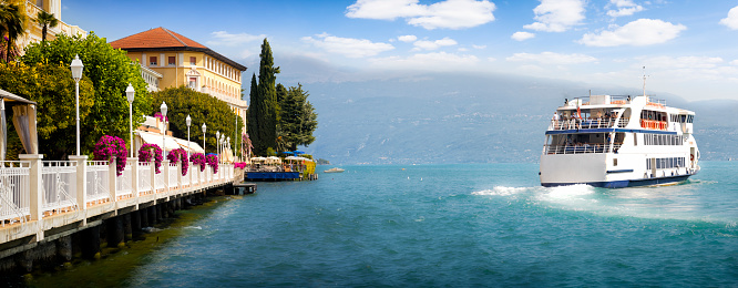 Holidays in Italy  - scenic view of the tourist town of Gardone Riviera and the departing ferry on Lake Garda