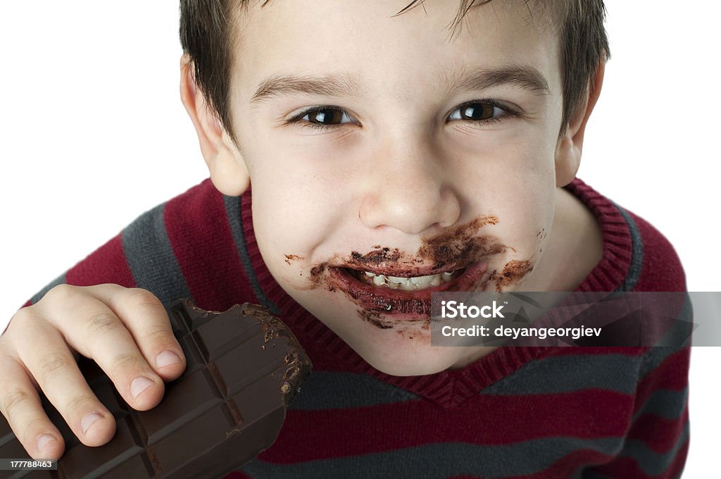 Smiling little boy eating chocolate Smiling kid eating chocolate. Smeared stained with chocolate lips. White isolated Addiction Stock Photo