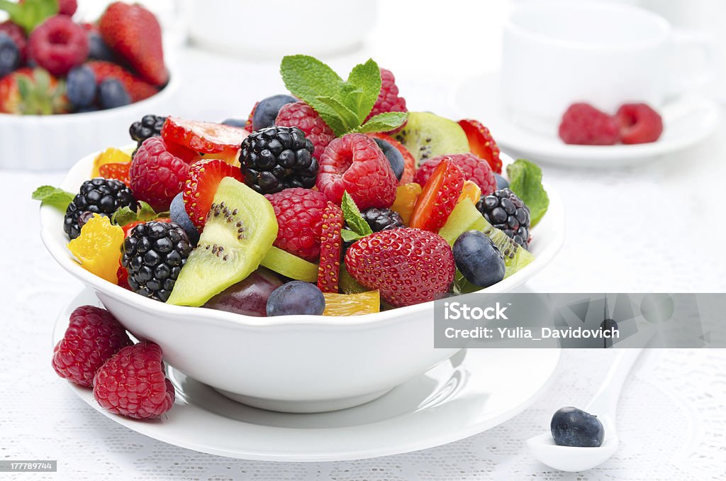 salad of fresh fruit and berries in a white bowl salad of fresh fruit and berries in a white bowl, berries and a cup of tea in the background, horizontal closeup Agriculture Stock Photo