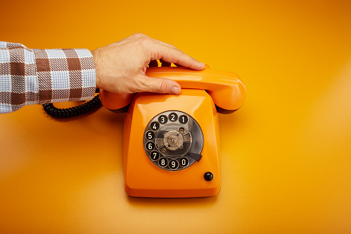 Getting a call. Hand picking up an old fashioned vintage telephone receiver and answering the phone call. Holding an orange retro phone receiver handset against orange background