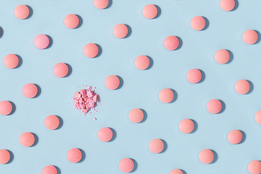 Pink pills with broken pills on soft blue background