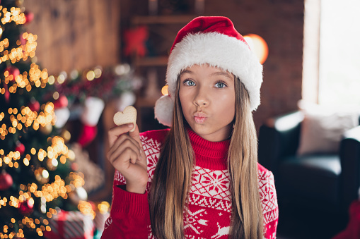 Photo of flirty funny small girl wear red print sweater lips pouted plump cooking new year xmas biscuits indoors house room.