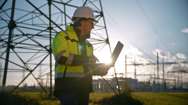 istock Sunlight Streaming Through Laptop Held By Electrical Engineer Looking Away At Power Station. As sunlight streams through,an electrical engineer holds a laptop while looking away at the power station,symbolizing the convergence of technology and expertise 1777961812