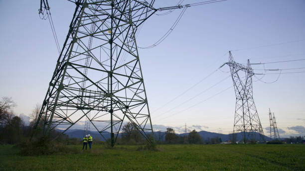 istock Electrical Engineers Standing Under Electricity Pylon On Grassy Field At Power Station. Engineers Under Electricity Pylon 1777962632