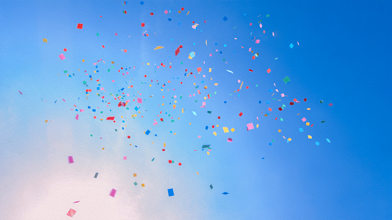 Colourful paper confetti falling against blue sky.