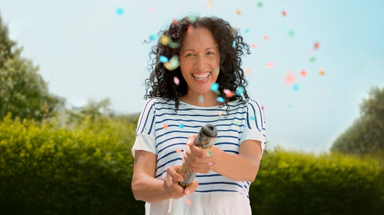 Portrait of smiling mature woman exploding confetti from party popper during event.