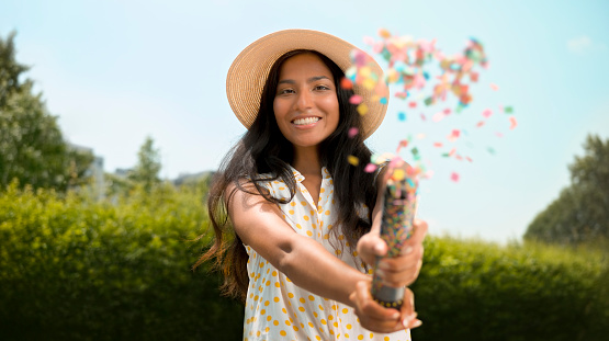 Portrait of smiling young woman exploding confetti from party popper during event.