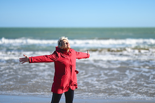 Senior woman standing in front to the sea with arms outstretch.