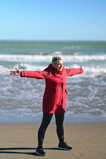 Mature woman in a windy beach standing with her arms outstretch.